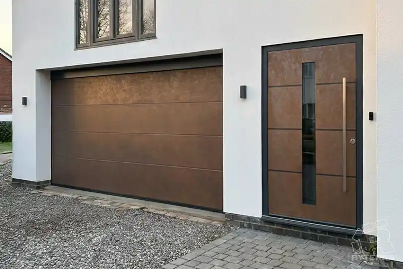 Tumšas ārdurvis ar koka dekora joslu un saskaņotiem brūniem garāžas vārtiem